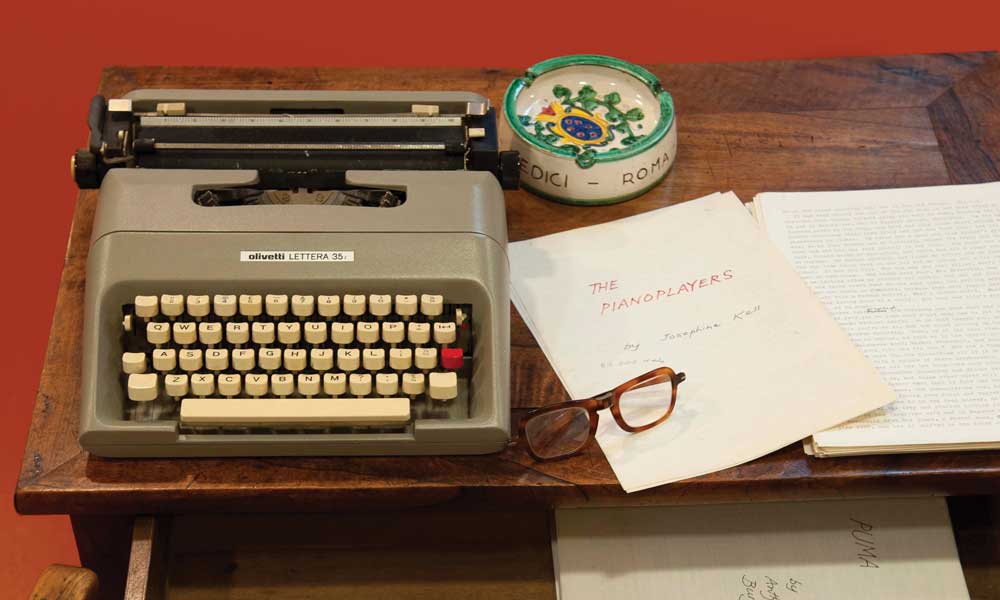 Photo of Anthony Burgess's writing desk, on top of the desk sits a typewriter, pair of glasses, ash-tray and some of his written work